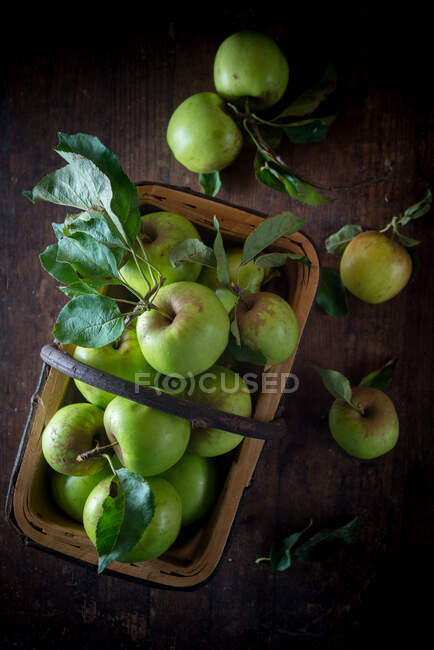 Vue de dessus du tas de petites pommes vertes entières avec des feuilles dans le panier sur la surface en bois — Photo de stock