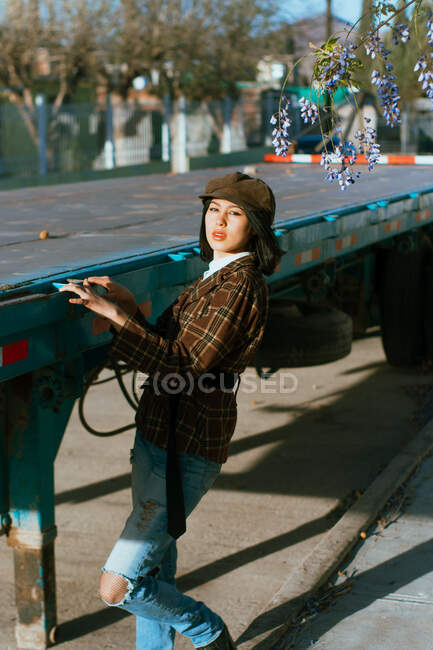 Side view of young stylish ethnic female in beret against aged trailer looking at camera in sunlight — Photo de stock