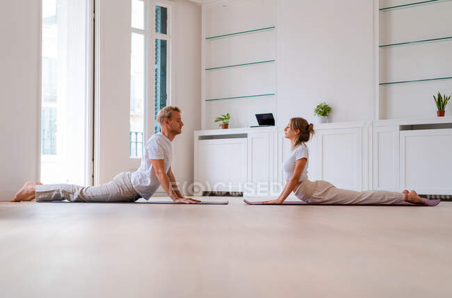 Ground level side view of serene couple practicing yoga in Bhujangasana in morning at home — Fotografia de Stock