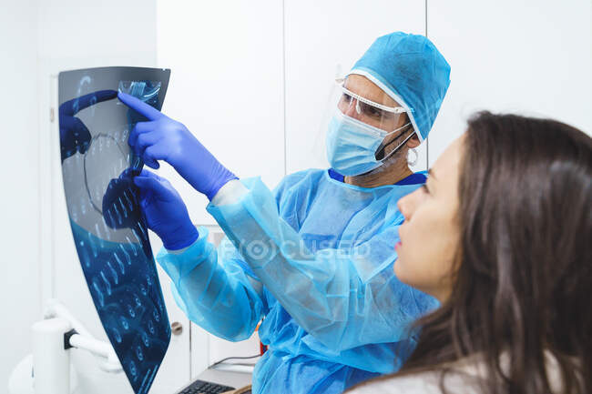Chirurgo maschio in uniforme che indica l'immagine radiografica mentre parla con donna delle colture durante il check-up in clinica — Foto stock