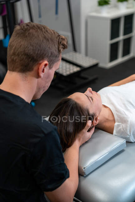 Von oben der unrasierte männliche Physiotherapeut, der Frau mit geschlossenen Augen im Krankenhaus den Hals massiert — Stockfoto
