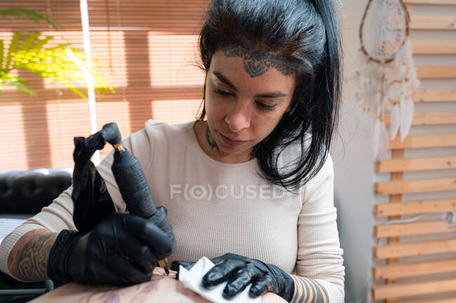 Tatuaje femenino con tatuaje de dibujo de máquina en el cuerpo del cliente irreconocible en el salón - foto de stock