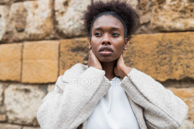 Portrait of attractive African American female with coat standing in historic city district on warm spring day and looking away — Stock Photo