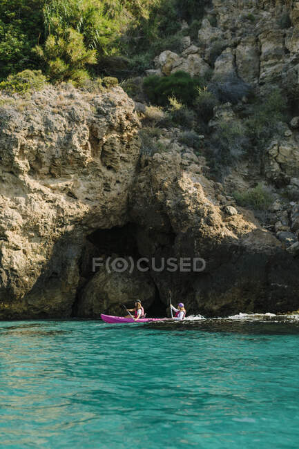 Side view anonymous travelers with paddles floating on turquoise seawater near the rocky shore on sunny day in Malaga Spain — Stock Photo