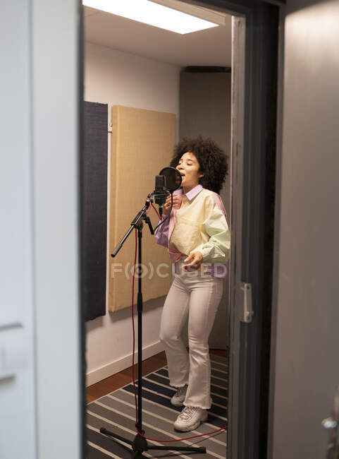 Cantora negra cantando música contra microfone com filtro pop em pé e olhos fechados no estúdio de som — Fotografia de Stock