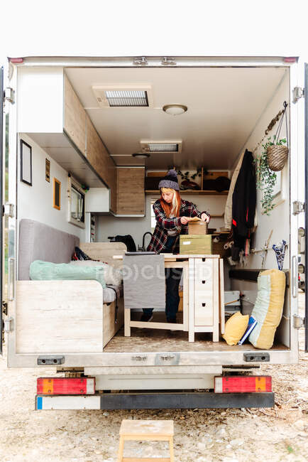 Мандрівний жіночий хіпстер, що стоїть у припаркованій вантажівці та упаковує різні речі під час поїздки влітку — стокове фото