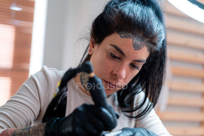 Female tattooer with machine drawing tattoo on body of unrecognizable client in salon — Stock Photo