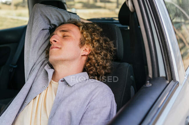 Relaxed young male traveler sleeping on driver seat of modern automobile while resting during road trip through countryside in summer day — Fotografia de Stock