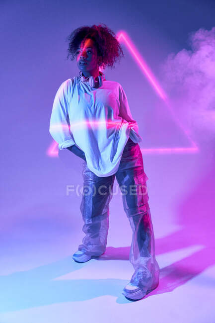 Confiante jovem dançarina afro-americana com cabelo encaracolado de pé olhando para longe em luzes de néon — Fotografia de Stock