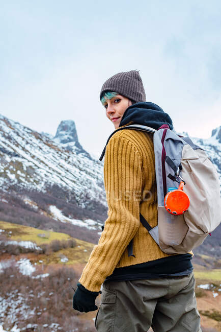 Vista lateral do caminhante com mochila e roupas quentes em pé no cume rochoso do vale em Peaks da Europa e olhando para a câmera — Fotografia de Stock