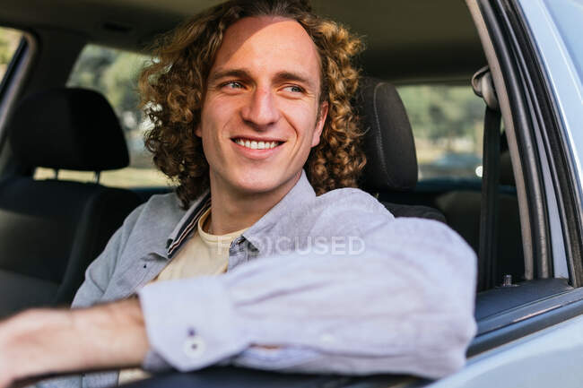 Щасливий молодий волохатий чоловік дивиться у відкритому вікні автомобіля, сидячи на водійському сидінні — стокове фото