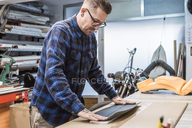 Seitenansicht eines gut aussehenden männlichen Kunsthandwerkers, der Stoffe verwendet und Polster für Motorradsitze in der Werkstatt herstellt — Stockfoto