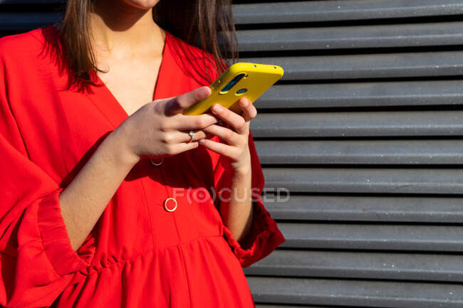 Junge Frau in Rot plaudert auf Handy im Sonnenlicht vor grauem Hintergrund — Stockfoto