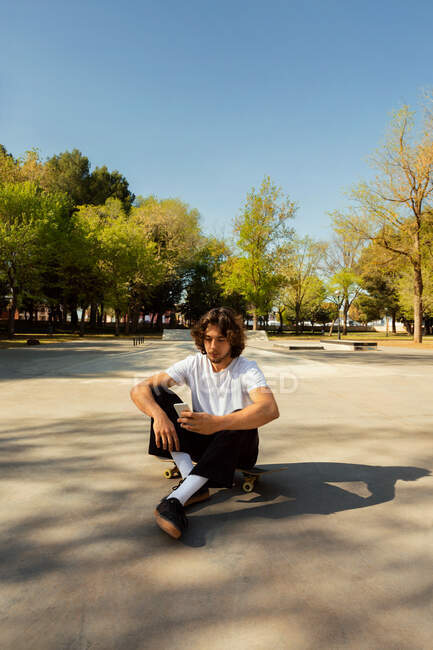 Porträt eines Skateboarders, der auf sein Handy blickt. Er hat die Kopfhörer auf den Schultern — Stockfoto