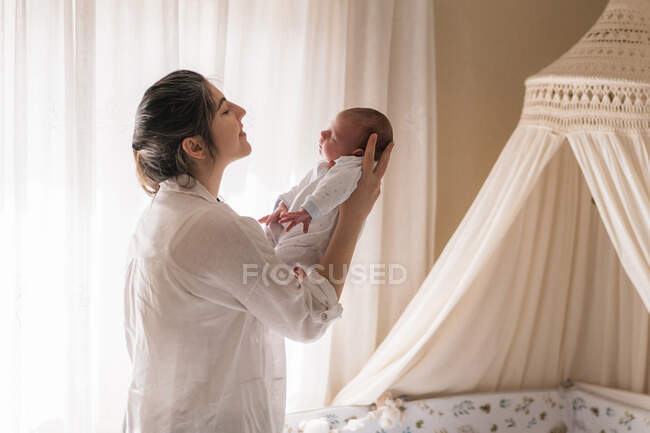 Mère souriante tenant et interagissant avec un petit enfant endormi à la maison en plein jour — Photo de stock