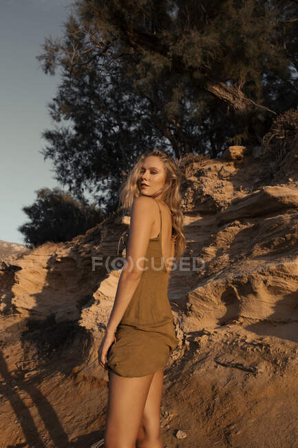 Crop of sensual blond female standing near sandy slope with grass plants — Stock Photo