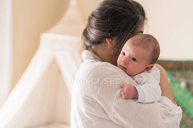 Неузнаваемая мама обнимает маленького ребенка дома при дневном свете — стоковое фото
