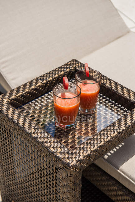 Glasses of fresh yummy watermelon squeezed juice served on small wicker rattan table near comfortable sunbed in tropical resort on sunny summer day — Stock Photo