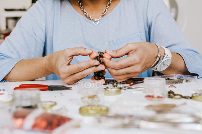 Front view of crop anonymous female master with instrument making necklace at table with different tools — Stock Photo