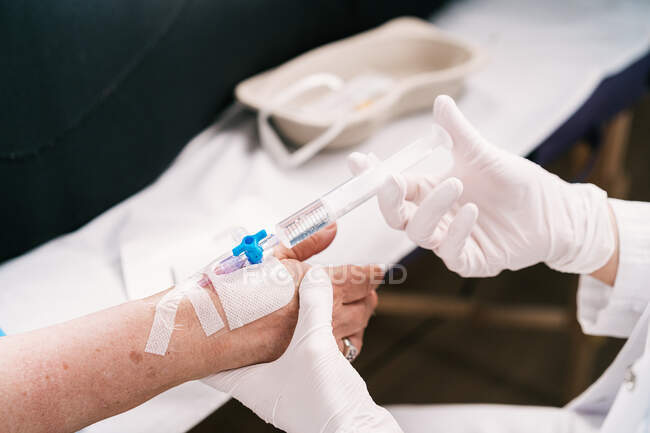 Colheita médica irreconhecível em luvas de látex injetando remédio no braço do paciente através de cateter intravenoso no hospital — Fotografia de Stock