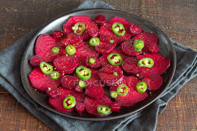 From above composition of tasty beetroot slices arranged on baking pan with green jalapeno peppers and placed on black towel on kitchen table — Stock Photo