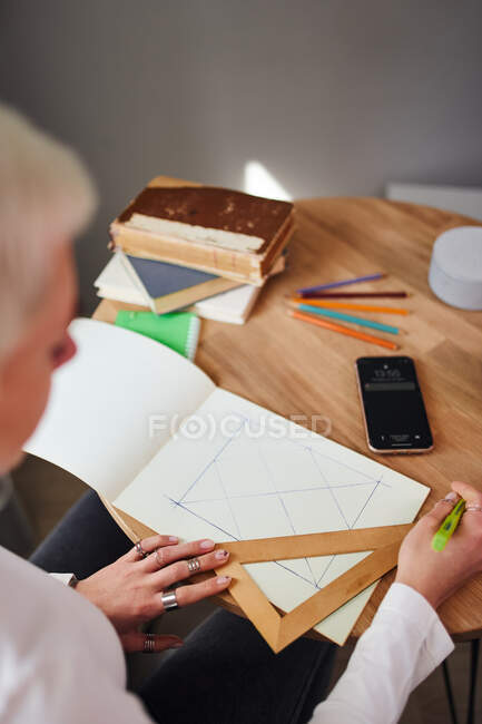 De arriba de la cosecha el dibujo irreconocible femenino astrólogo sobre el papel con el triángulo y la pluma a la mesa - foto de stock