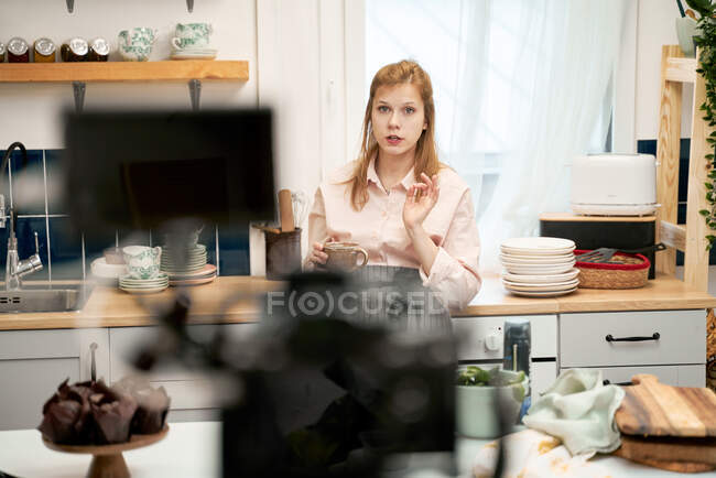 Молодая блоггер говорит против смартфона во время записи кулинарного видео и смотрит в камеру дома — стоковое фото