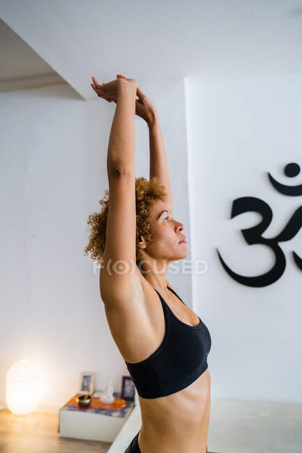 Vista laterale di tranquilla femmina etnica con acconciatura afro in piedi in posa Montagna con le braccia alzate e facendo yoga in studio — Foto stock