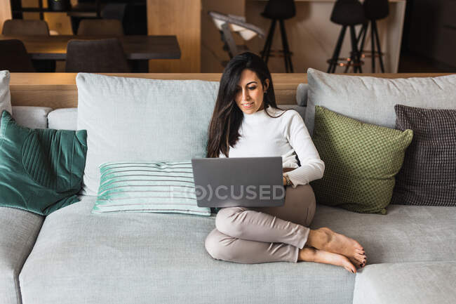 Brünette Frau sitzt auf bequemem Sofa und surft am Wochenende zu Hause auf Netbook im Internet — Stockfoto
