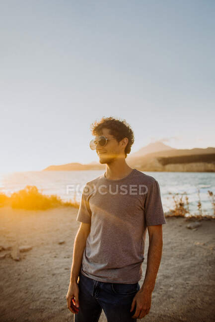 Side view male traveler in casual clothes and sunglasses clapping hands on sandy seacoast at picturesque sunset while spending summer vacation in Fyriplaka Greece — Stock Photo