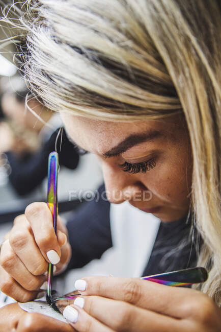 Female beauty master with tweezers applying fake eyelashes on face of cropped unrecognizable ethnic client in salon — Foto stock