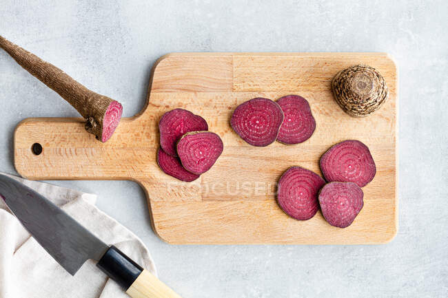 Zusammensetzung von reifen rohen Rote-Bete-Scheiben auf einem Holzschneidebrett auf dem Küchentisch in der Nähe eines scharfen Messers — Stockfoto