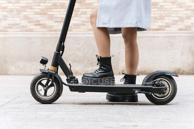 Cropped unrecognizable female in casual wear riding scooter on paved sidewalk — Photo de stock