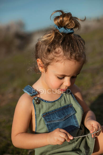 Зачарована чарівна дівчинка в комбінезоні стоїть на лузі і дивиться вниз — стокове фото