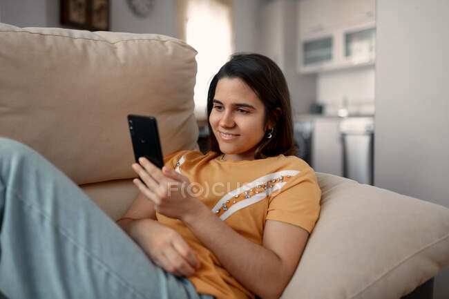 Молодая женщина смс-ки на мобильный телефон, лежа на диване в гостиной — стоковое фото