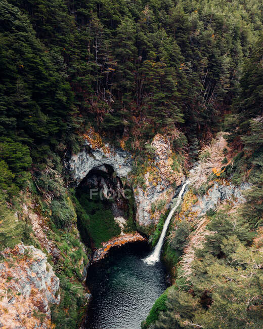 Захватывающий вид беспилотника на мощный поток водопада, текущий в озере в горных лесах — стоковое фото