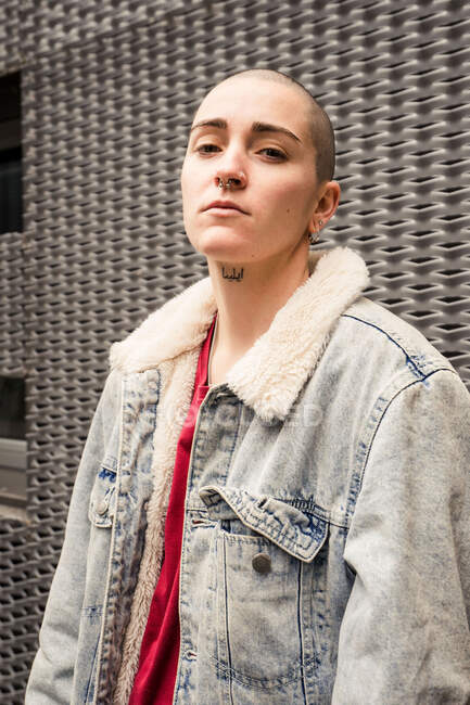 Трансгендер в джинсовой куртке с мехом и серьгами смотрит в камеру при дневном свете — стоковое фото