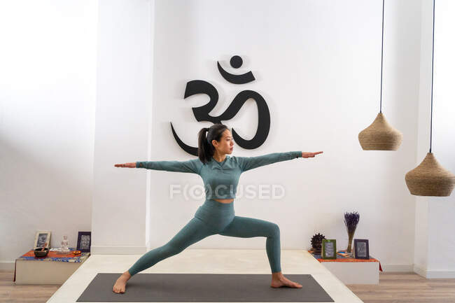 Graciosa etnia feminina em pé em Virabhadrasana e praticando ioga no tapete em estúdio — Fotografia de Stock