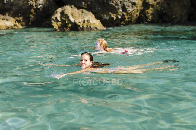 Mujeres amigas relajadas nadando tranquilamente en el cálido agua de mar azul cerca de la costa en un día soleado en Málaga España - foto de stock