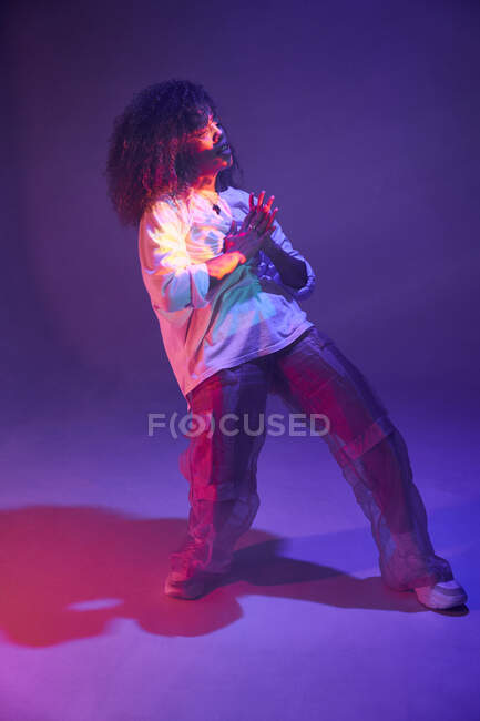 Full body attractive young African American female in loose informal clothes dancing in dark studio in neon lights — Stock Photo