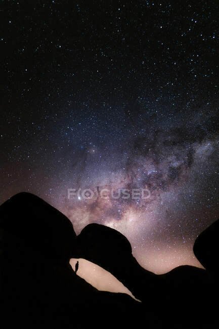 Silhouette de touriste anonyme debout sur une falaise et admirant les étoiles brillantes rayonnant sur le ciel nocturne — Photo de stock