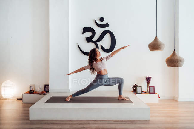 Изысканная молодая женщина, стоящая в Вирабхадрасане и практикующая йогу на коврике в студии — стоковое фото