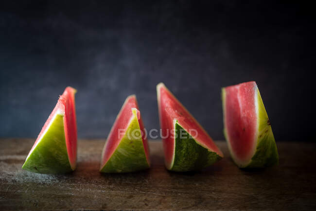 Delicious ripe watermelon slices with juicy pulp in row on wooden surface on blurred background — Stock Photo