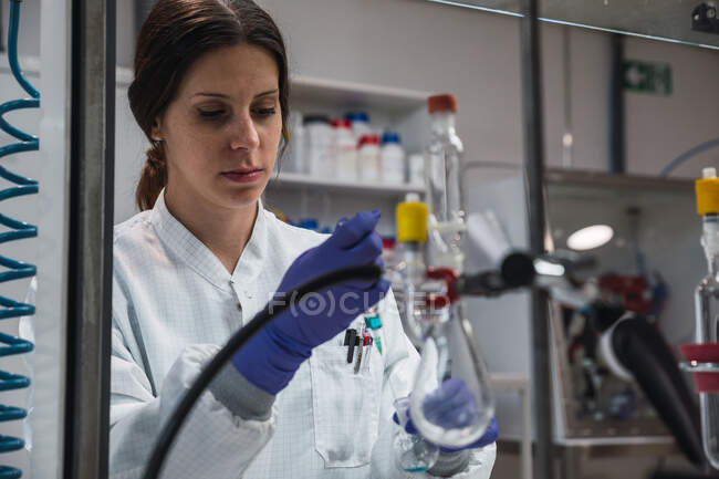 Кроп концентрувала жіночу науку в білому одязі і рукавичках, проводячи хімічний експеримент з речовиною і шприцом під час роботи в сучасній лабораторії. — стокове фото