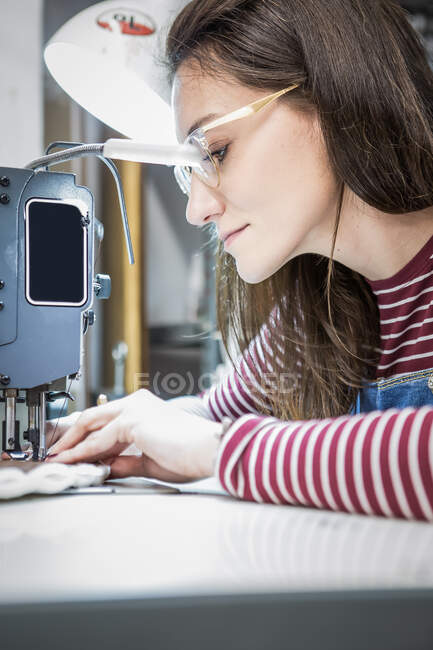 Artesana vista lateral usando máquina de coser mientras crea tapicería para asiento de moto en taller - foto de stock