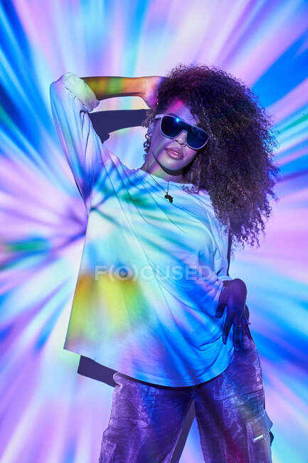 Stylish confident African American female dancer with curly hair in sunglasses standing in neon lights in dancing studio — Stock Photo