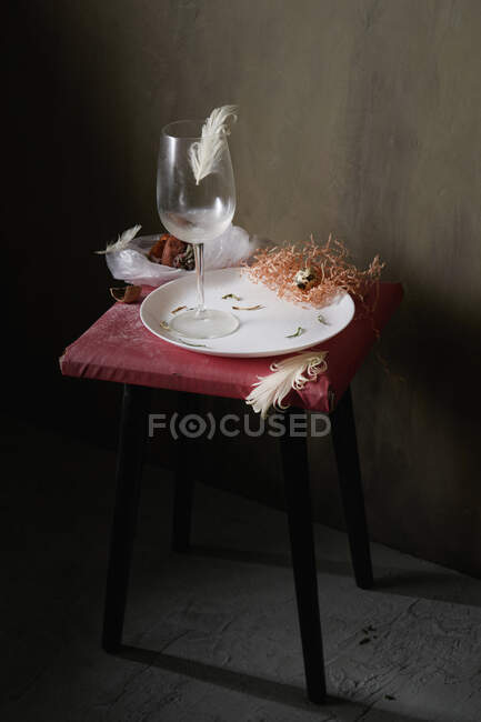 Transparent glass on round shaped ceramic plate with cardboard shavings on stool in building — Stock Photo