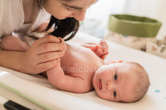 Schnitte anonyme Mutter legt Windel auf charmante kleine Kind Blick auf Kamera auf Säugling Tisch im Haus — Stockfoto