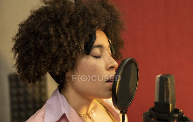 Cantante nera che canta contro il microfono con filtro pop in piedi e gli occhi chiusi in studio sonoro — Foto stock