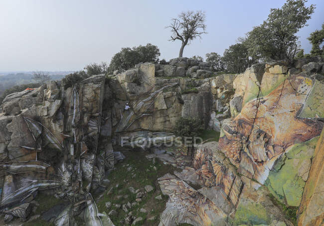 Drone view of man in helmet hanging on rope while painting graffiti on steep stony slope — Stock Photo